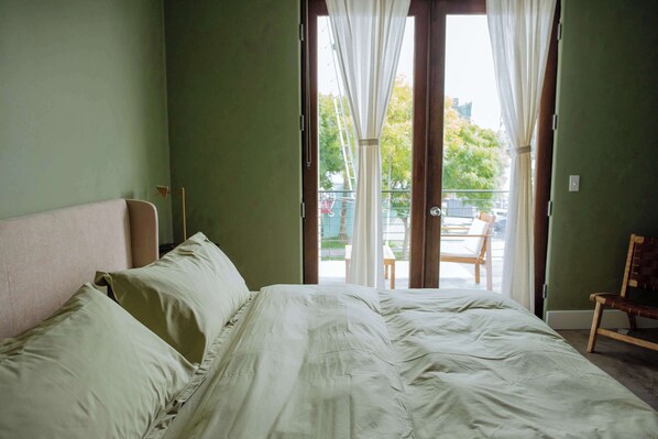 Un dormitorio con cama, una silla y vistas a un balcón exterior.