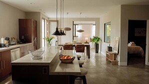 Eine moderne Küche mit Kochinsel, Pendelleuchten und einem Essbereich mit Blick zum Wohnzimmer.