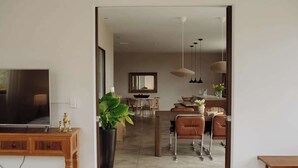 Ein modernes Wohnzimmer mit Fernseher, Holzschrank, Topfpflanze, Essbereich mit Stühlen und einer Küche im Hintergrund.