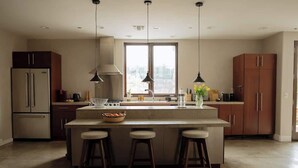 Eine moderne Küche mit Kochinsel, Barhocker, Kühlschrank und Pendelleuchten.