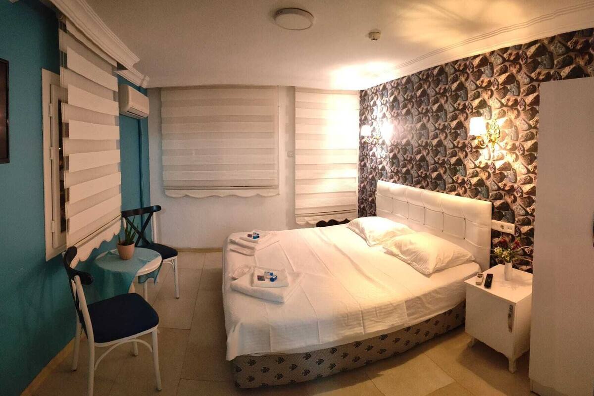 Une chambre à coucher avec un lit, une chaise, une petite table, une armoire et un mur en pierre.