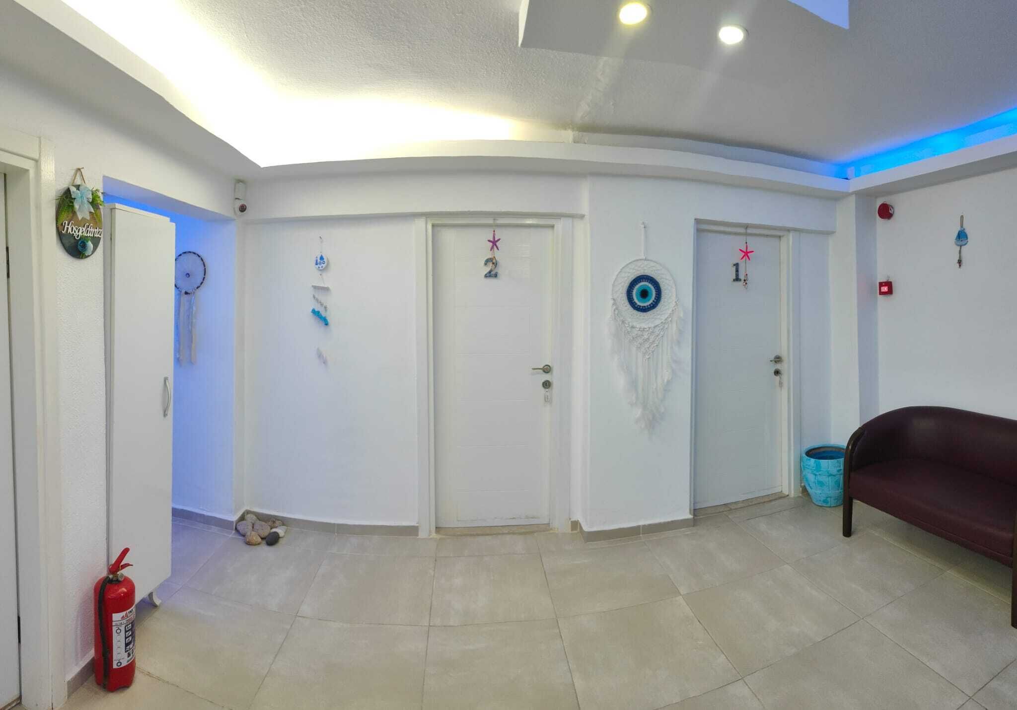 A spacious room with white walls, a red fire extinguisher, a blue trash bin, and a dark-colored sofa.