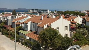 A residential area with houses, a clear sky, and a distant view of a body of water. - Dafne Butik Pansiyon (Karaburun)