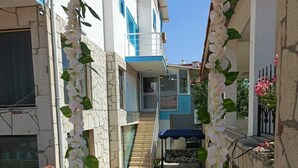 A narrow alleyway with a staircase leading to a building entrance, surrounded by white flowers and greenery. - Dafne Butik Pansiyon (Karaburun)