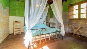 A room with a four-poster bed, a small wooden ladder, a stone wall, and a window with a wooden shutter. - Casa Vacanze La Casala (Fivizzano)