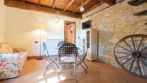 A rustic room with a wooden ceiling, a stone wall, a large wheel, a sofa, and a table with chairs. - Casa Vacanze La Casala (Fivizzano)