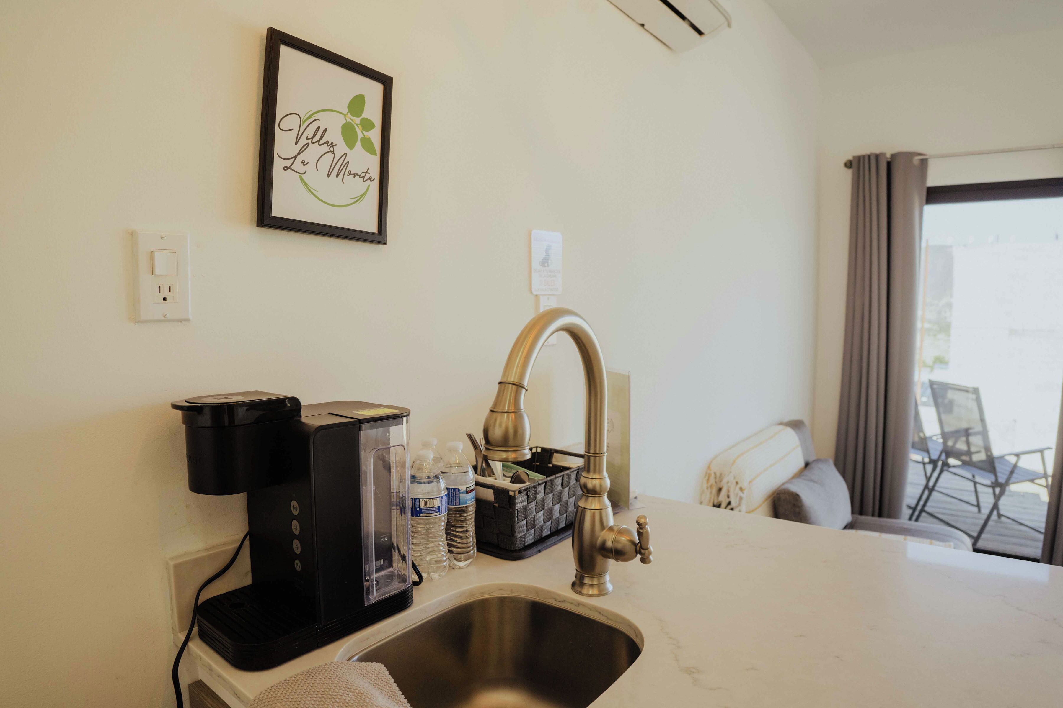 A kitchen with a coffee maker, a sink, and a framed sign on the wall.