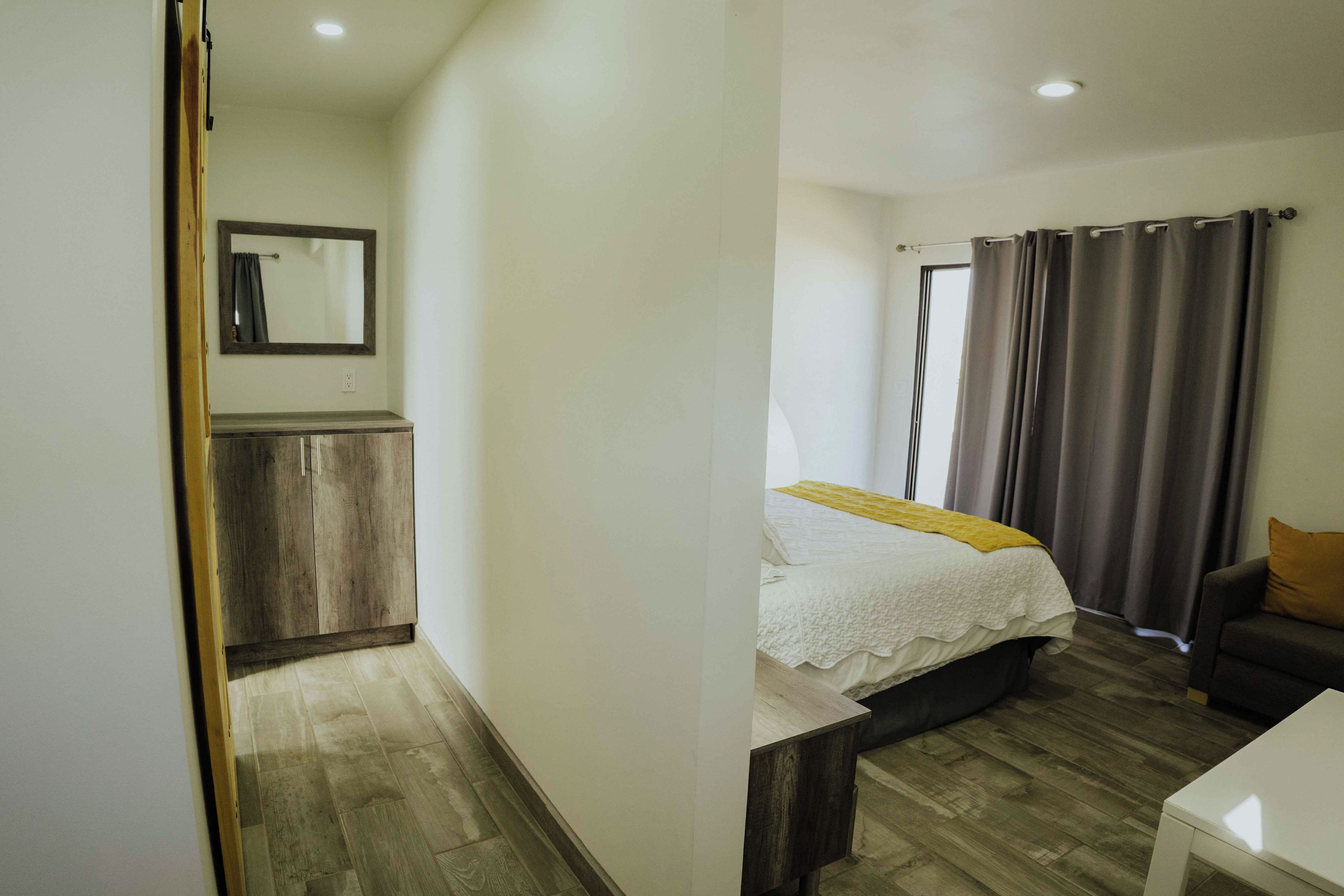 Quarto com cama, mesa de cabeceira, cadeira, guarda-roupa e janela com cortinas.