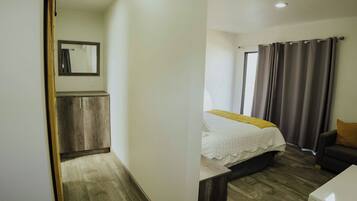Quarto com cama, mesa de cabeceira, cadeira, guarda-roupa e janela com cortinas.