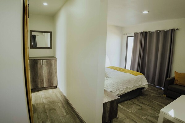 Un dormitorio con cama, mesita de noche, una silla, armario y ventana con cortinas.