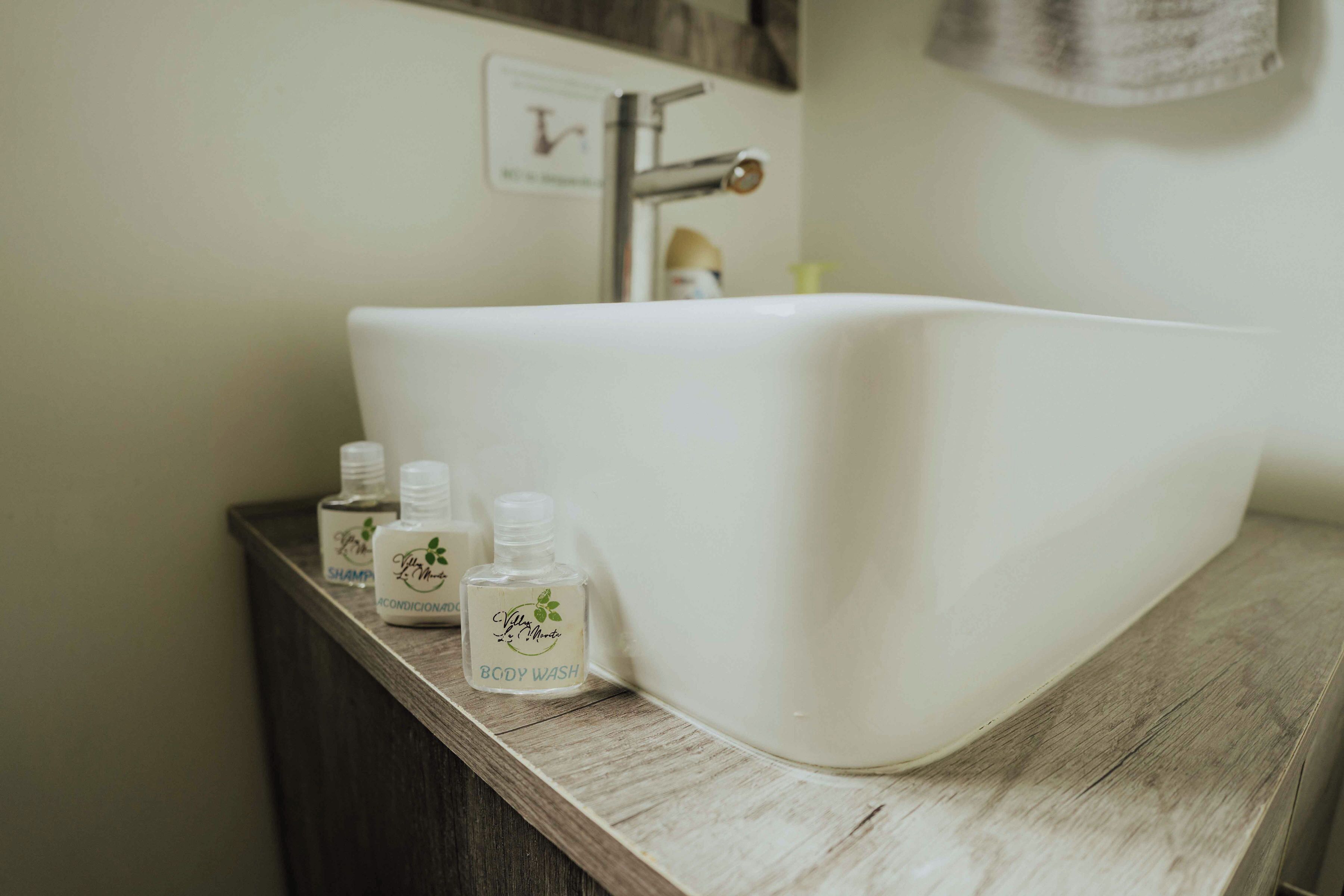 A bathroom with a white sink, wooden countertop, and three bottles of body wash.