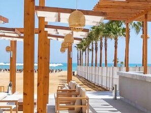 A wooden pergola with hanging lanterns overlooking a beach with palm trees and a clear view of the ocean. - Whispering Waters, Two Bedroom With a Garden, Azha (Ataqah)