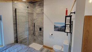 Ein modernes Badezimmer mit einer gläsernen Duschkabine, einer Toilette und einem kleinen Ablagebereich für Pflegeprodukte.