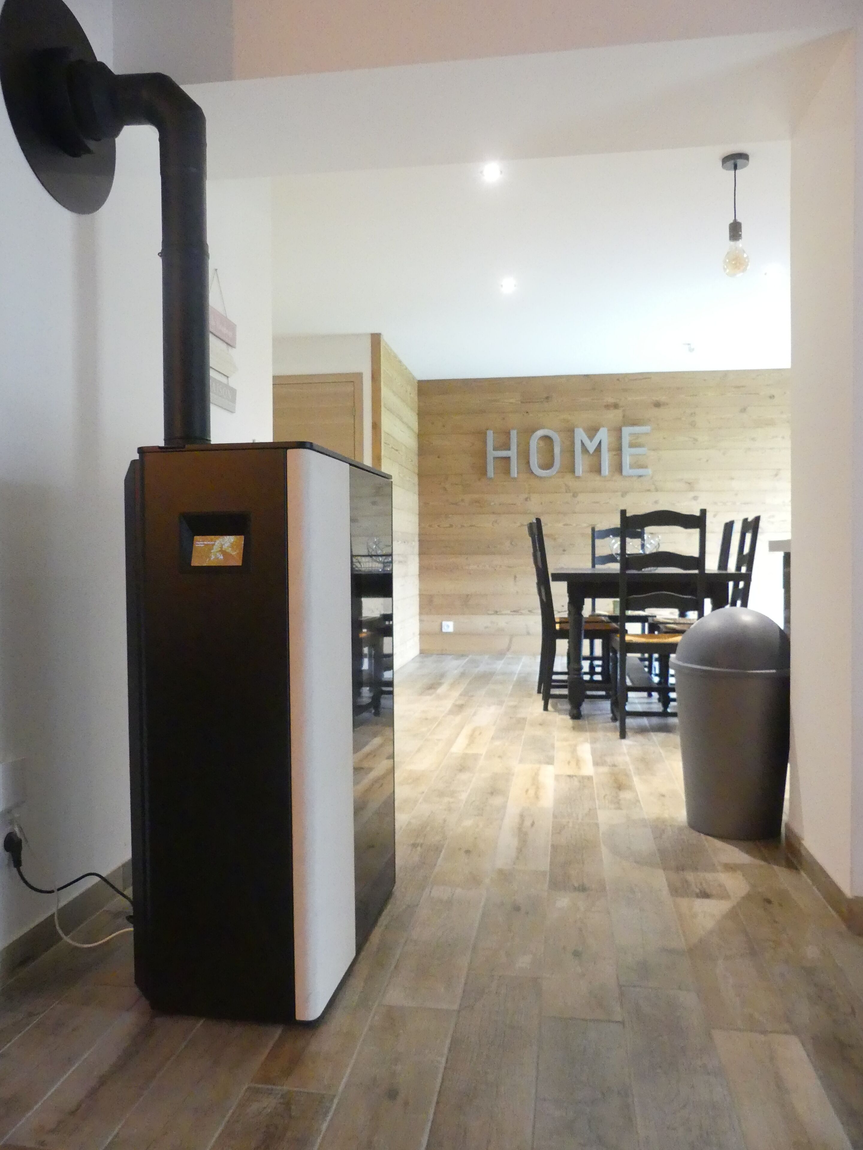 A modern kitchen with a built-in stove, a dining area with a wooden wall and a 'HOME' sign, and a trash bin.