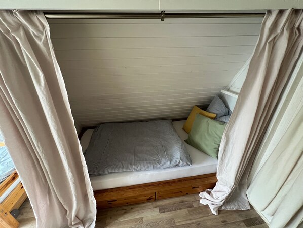 A small, cozy bed with striped bedding and a wooden platform, surrounded by light-colored curtains.