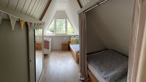 A bedroom with a sloped ceiling, a window, a bunk bed, a bedside table with a lamp, and a wooden floor. - Familienfreundliches Domizil am Großen Meer mit Stangenofen. Haustierfreundlich! (Südbrookmerland)