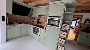 A modern kitchen with built-in appliances, a wooden ceiling, and light green cabinetry. - Familienfreundliches Domizil am Großen Meer mit Stangenofen. Haustierfreundlich! (Südbrookmerland)