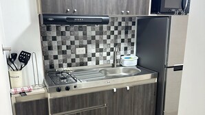 A compact kitchen with dark wood cabinets, a tiled backsplash, a gas stove, and a stainless steel refrigerator. - Encantador Loft en Medellín (Medellin)