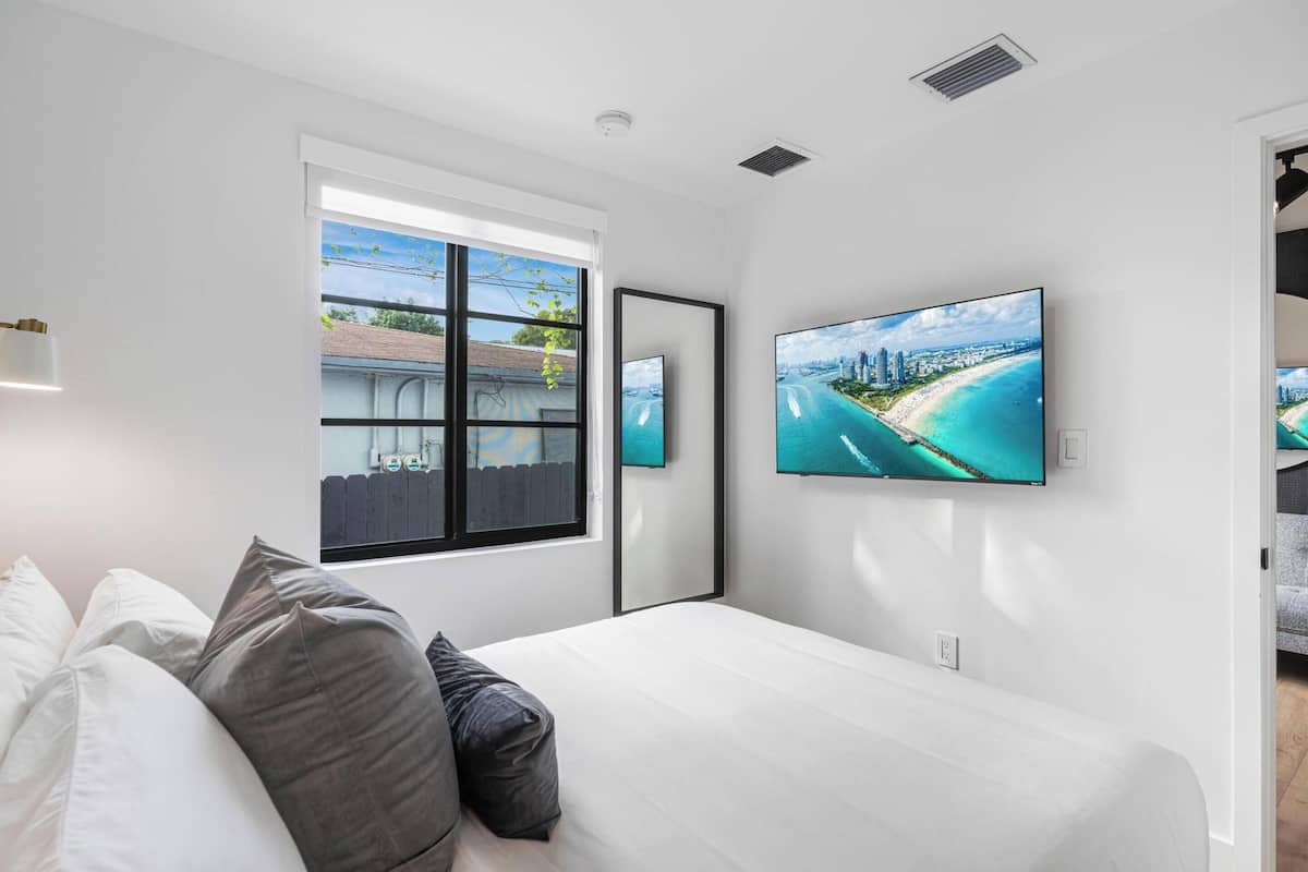 Ein Schlafzimmer mit einem großen Bett, einem Fenster mit Blick auf einen Strand und einem an der Wand montierten Fernseher.