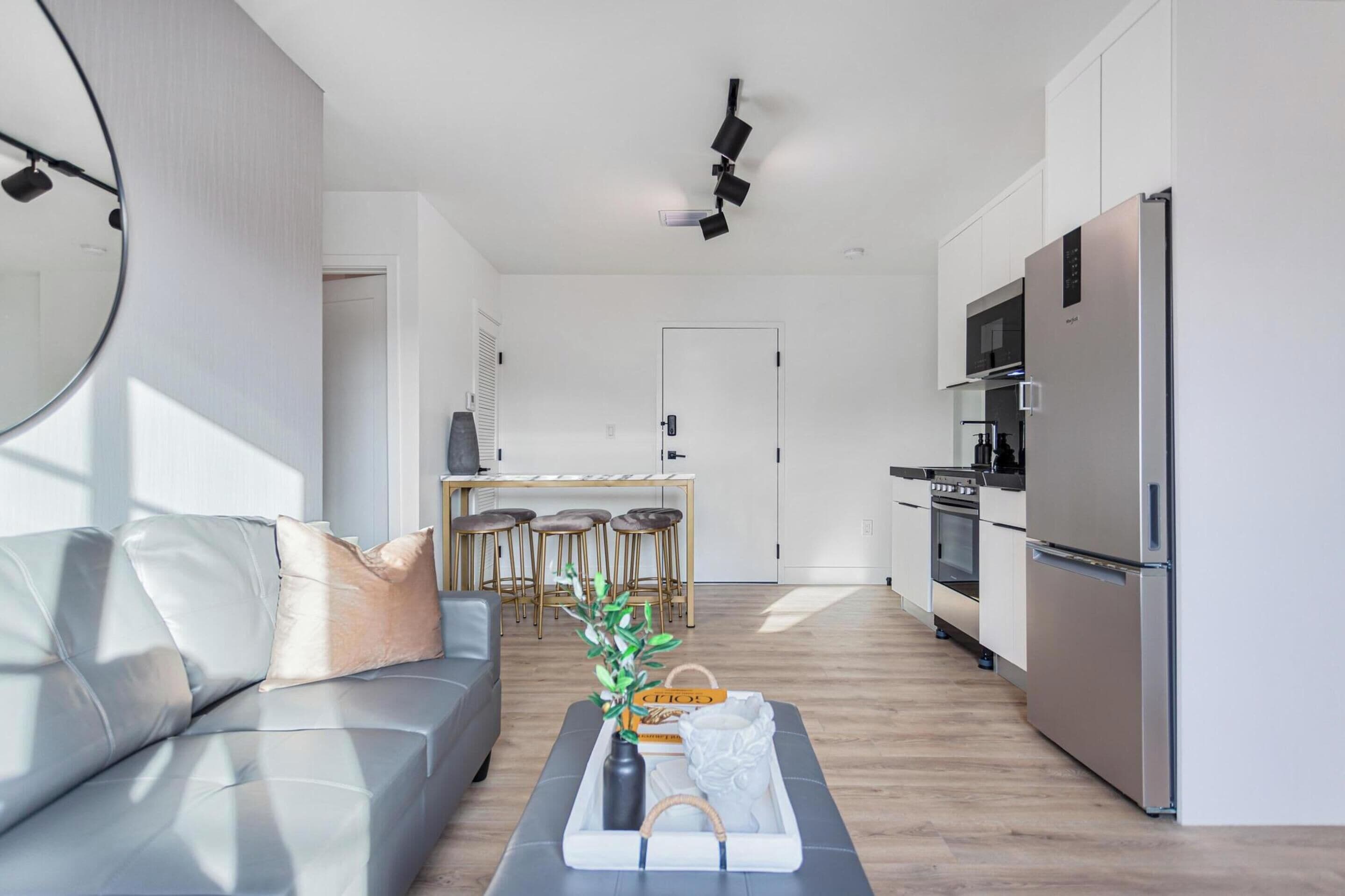 A modern kitchen with a stainless steel refrigerator, microwave, and oven. There is a dining area with a wooden table and chairs.