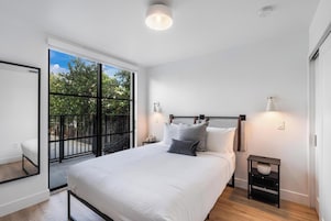 Una camera da letto moderna con un letto grande, un tavolino e un comodino, e vista sull'esterno attraverso una porta scorrevole.