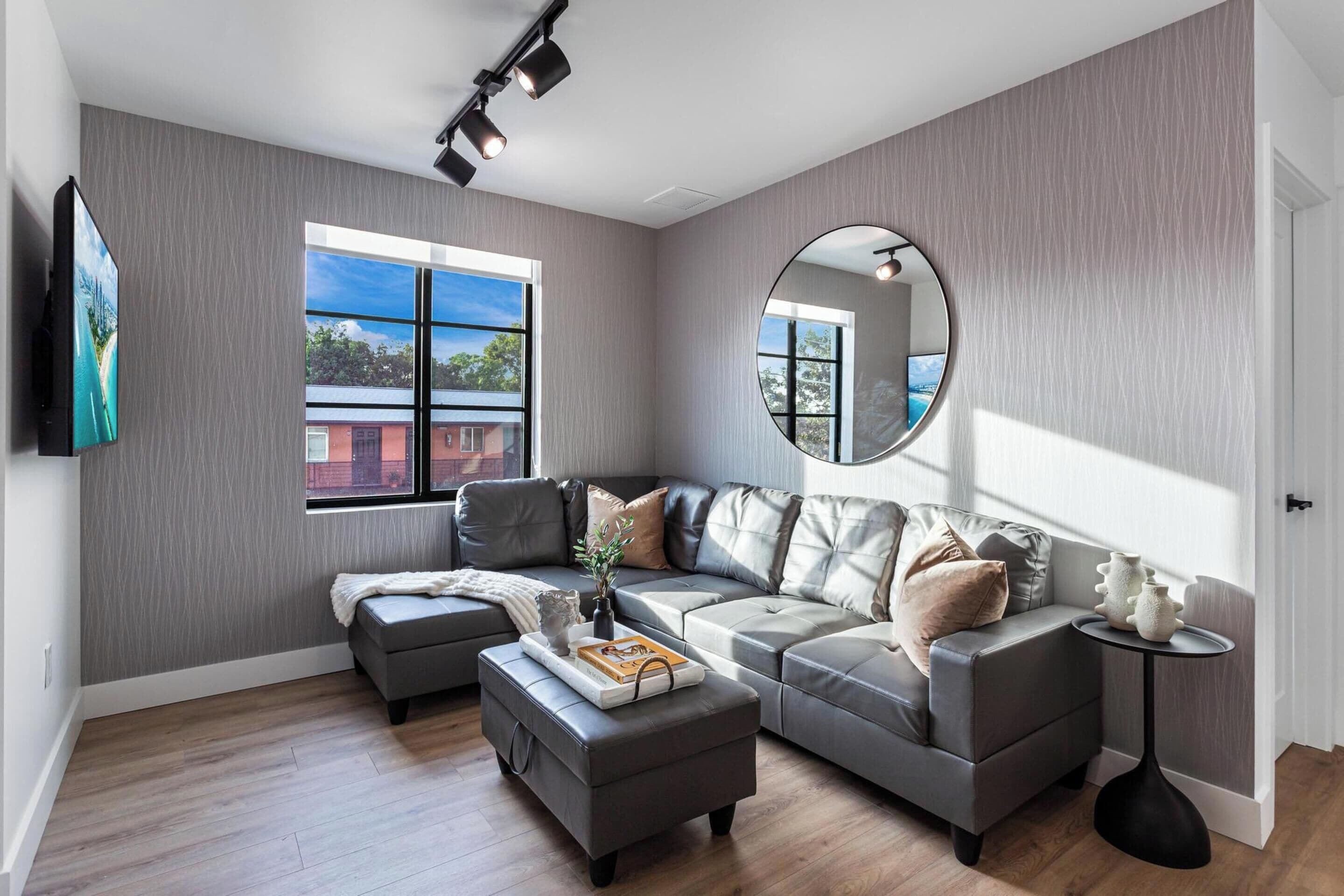 A modern living room with a sectional sofa, a round mirror, and a small side table.