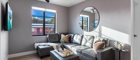 A modern living room with a sectional sofa, a round mirror, and a small side table.