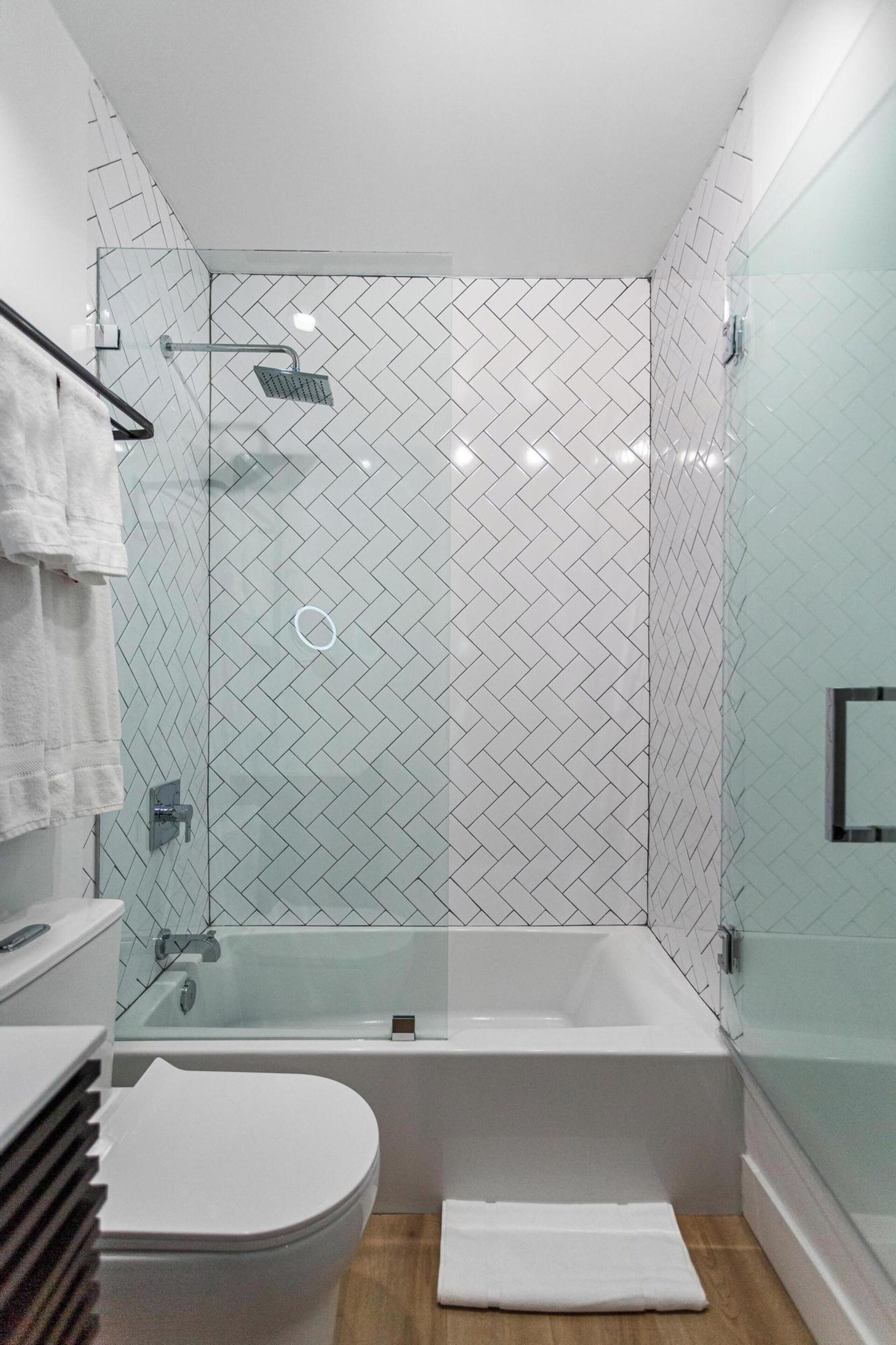 A modern bathroom with a glass-enclosed shower, a white bathtub, and a toilet.