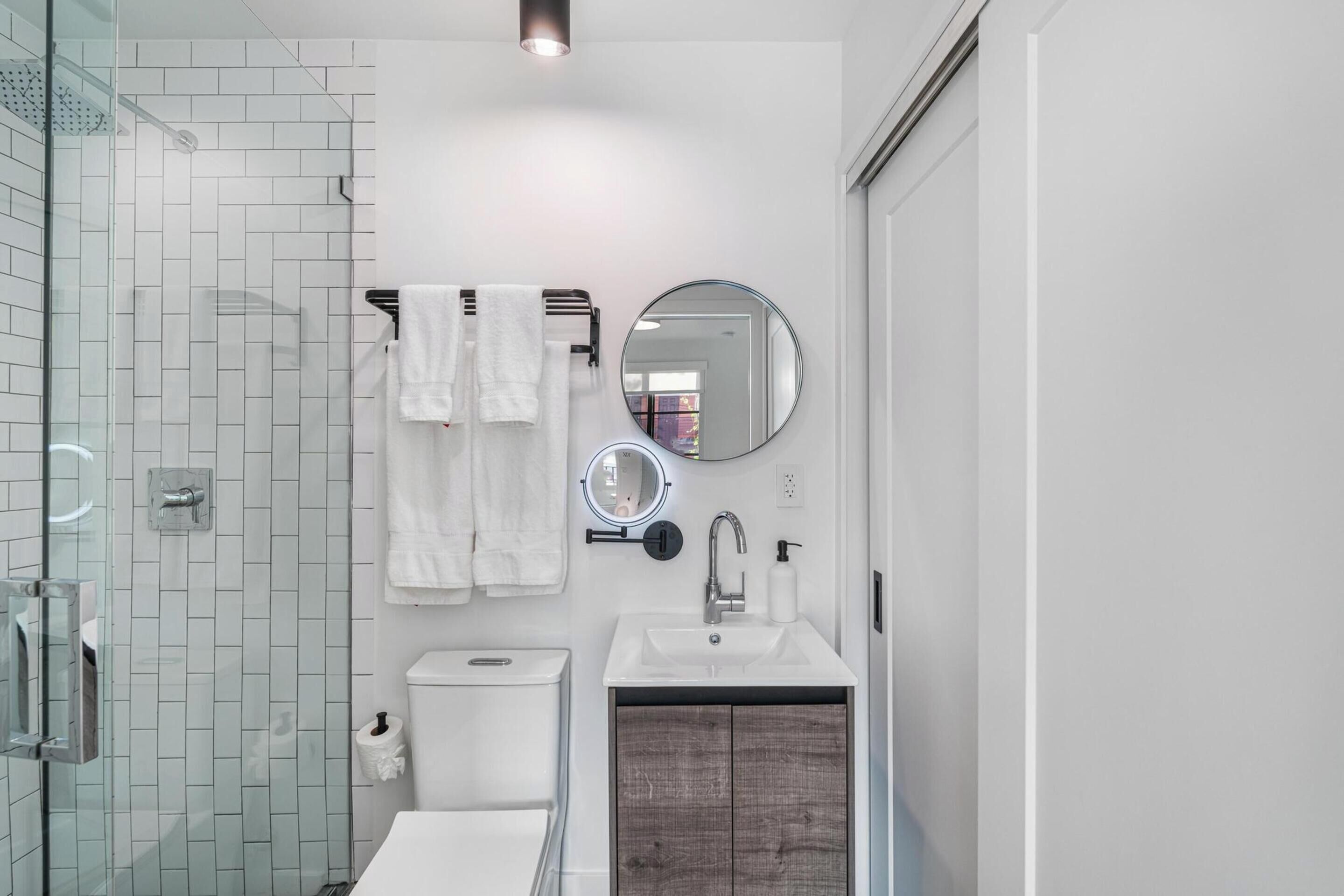 Une salle de bain moderne avec une douche à l’italienne en verre, un lavabo blanc et un meuble-lavabo en bois.