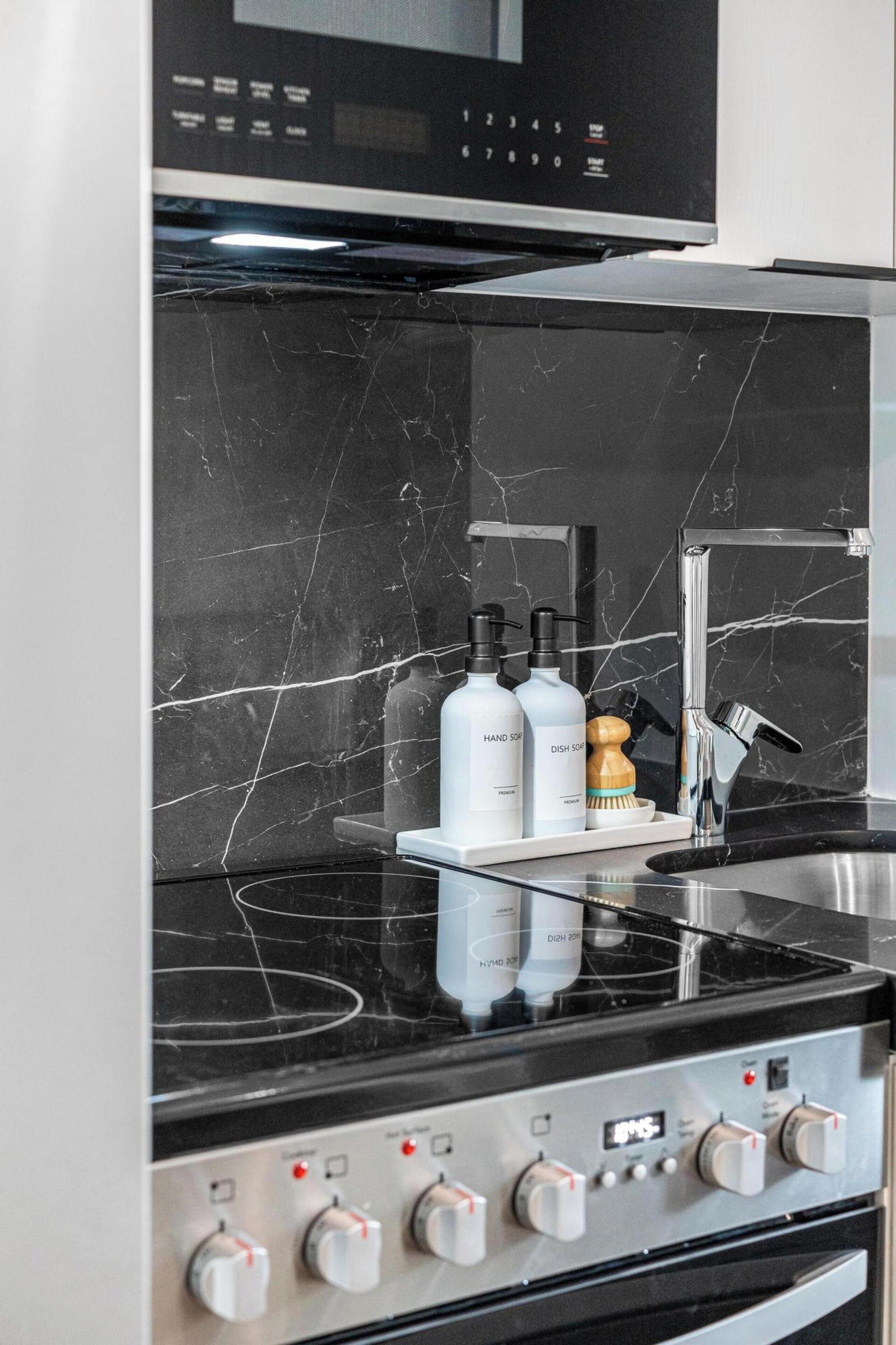 Une cuisine dotée d’un plan de travail en marbre noir, d’un évier en acier inoxydable et d’un four encastré avec des boutons de commande.
