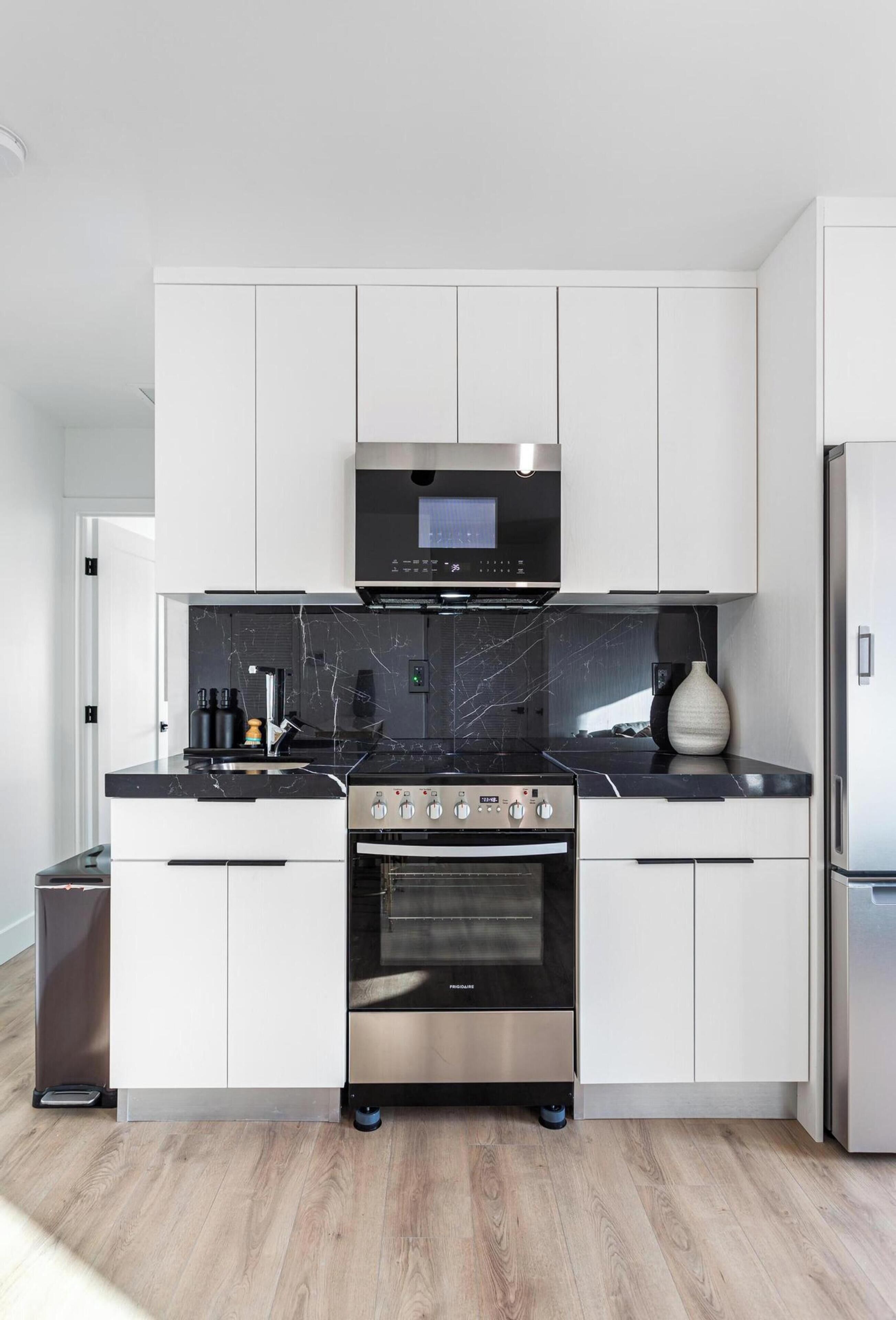 Een moderne keuken met witte kastjes, een zwart aanrecht, een RVS-fornuis en een magnetron.
