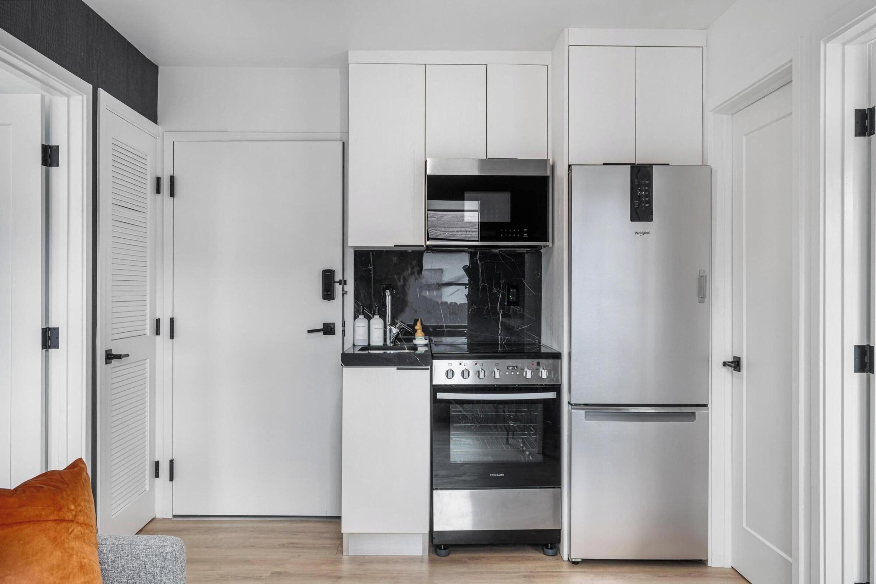 Una cocina moderna con armarios blancos, horno empotrado y refrigerador de acero inoxidable.