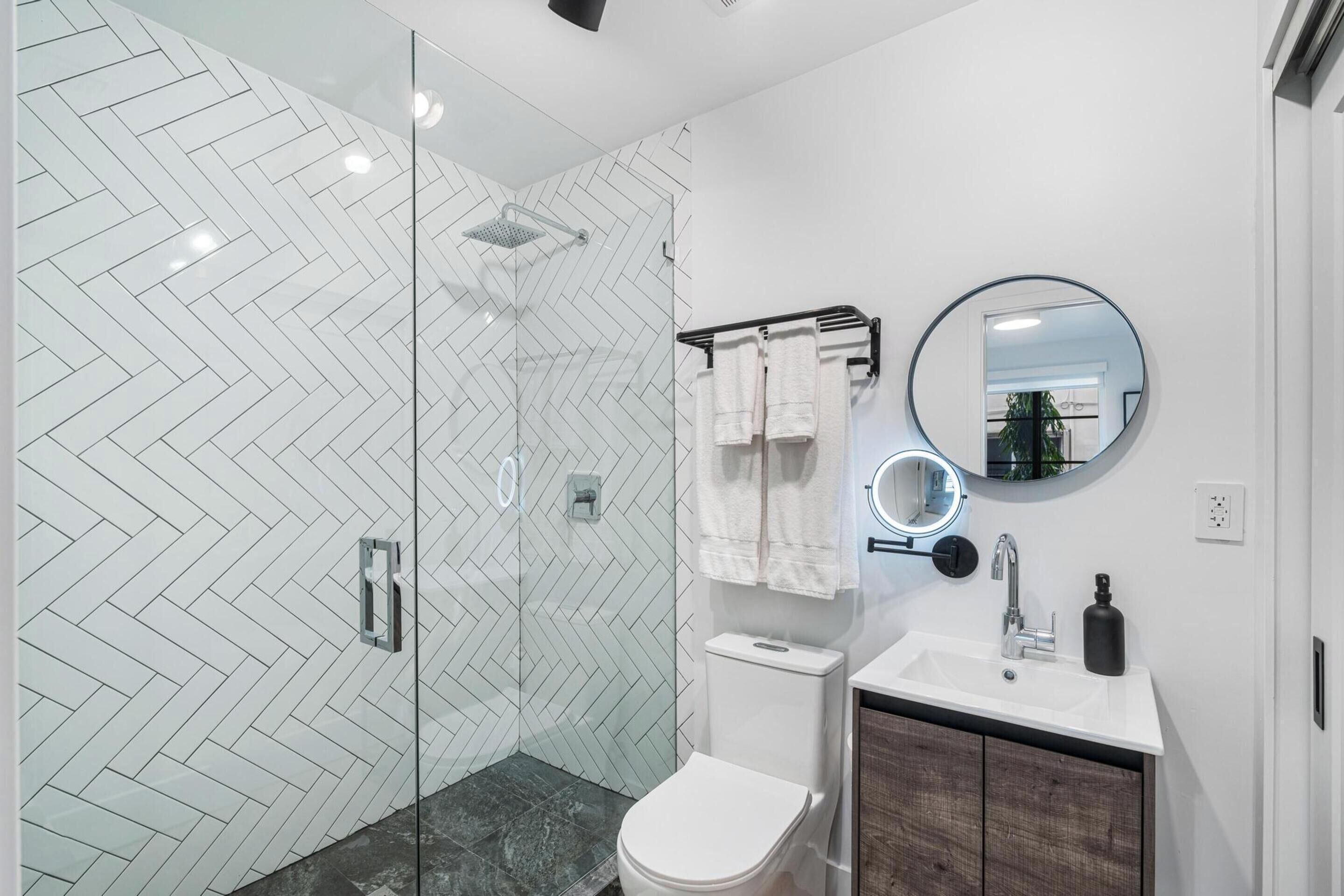 A modern bathroom with a glass shower enclosure, a white toilet, a sink with a mirror, and a towel rack.