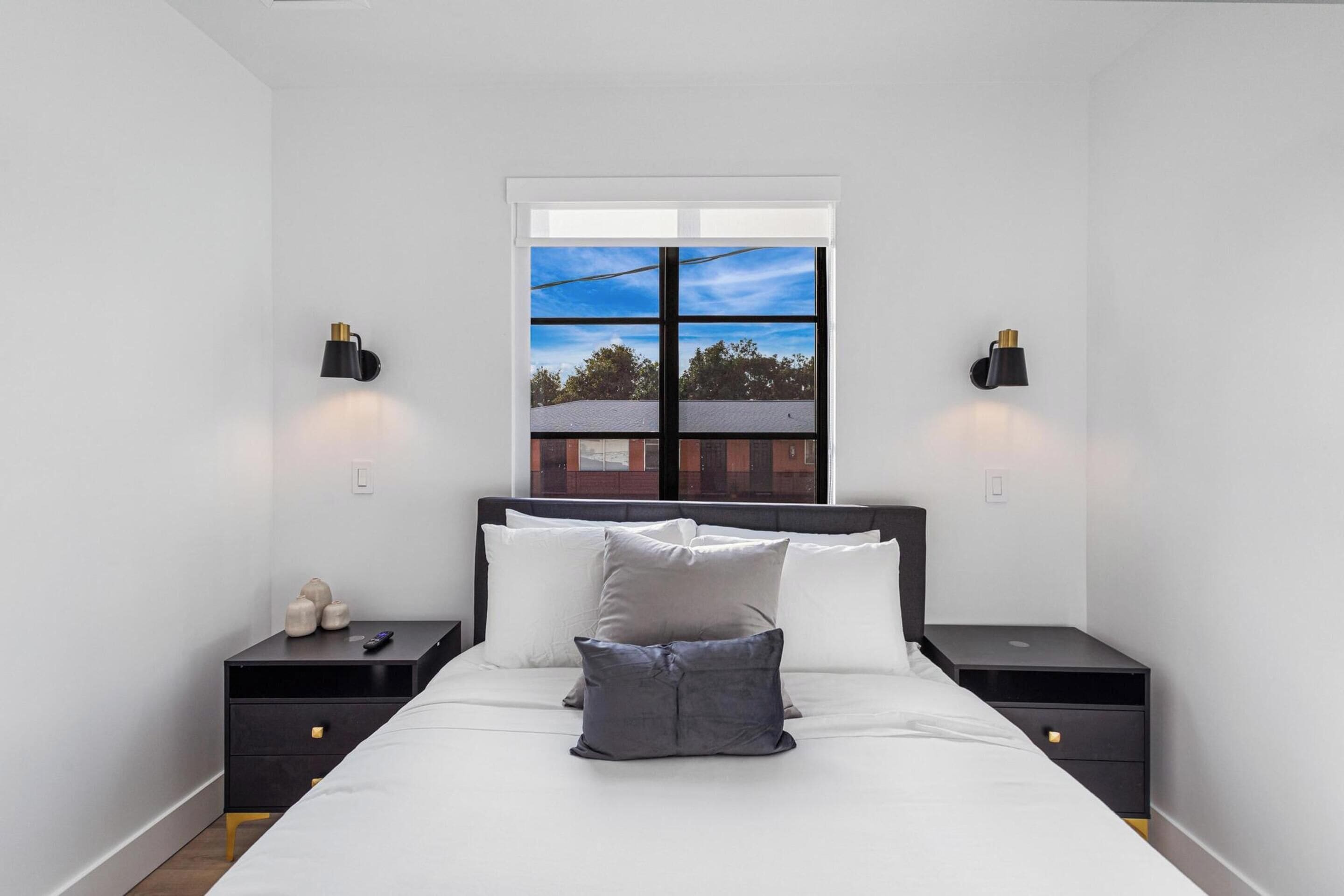 Ein Schlafzimmer mit einem großen Bett, zwei Nachttischen, einem Fenster mit Blick und Wandleuchten.