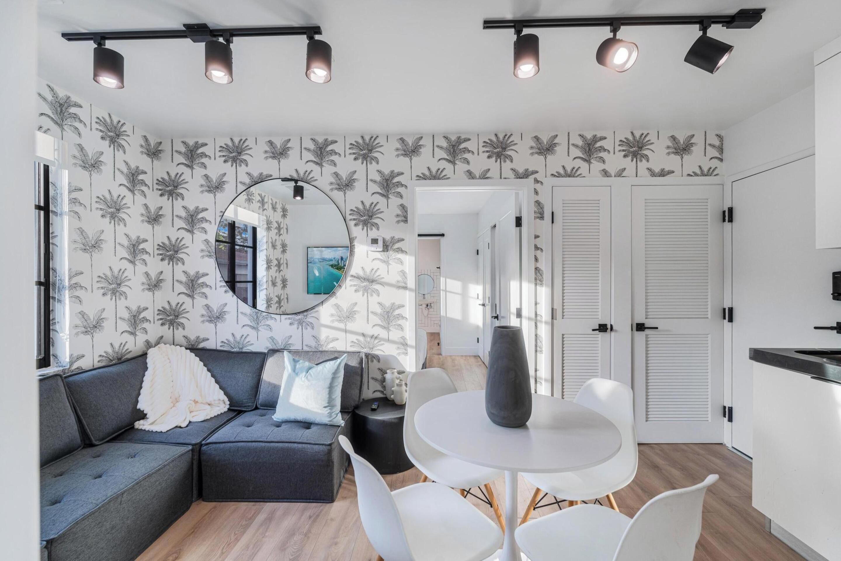 Uma sala de estar moderna com um sofá modular cinza, um espelho redondo e uma mesa de jantar branca.