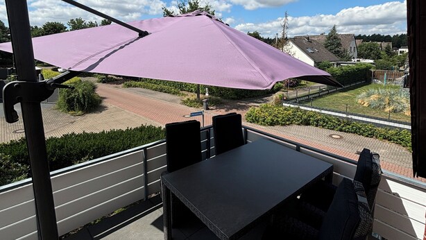 An outdoor patio with a table and chairs, a purple umbrella, and a view of the surrounding area.