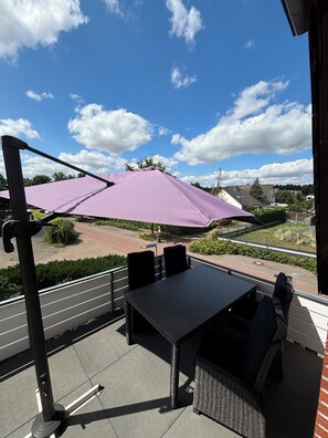 Un patio exterior con mesa y sillas, un paraguas morado y vistas del entorno.