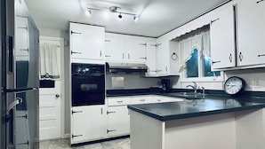 A kitchen with white cabinets, a black countertop, a stainless steel refrigerator, a built-in oven, and a clock on the wall. - Charming 3-bedroom ranch 1 minute from Mohegan Sun. (Montville)