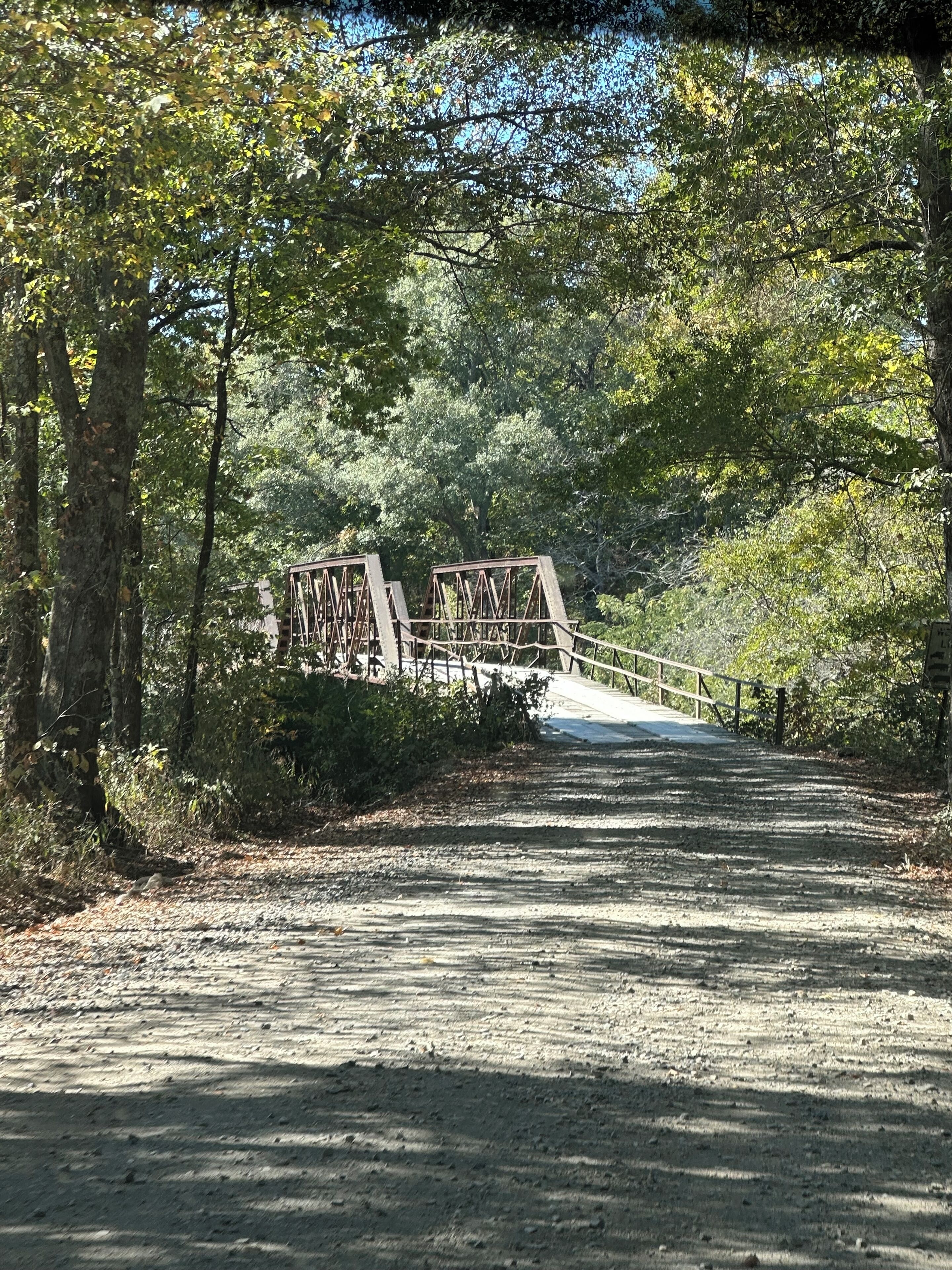Un sendero de grava que conduce a un puente metálico en una zona boscosa.