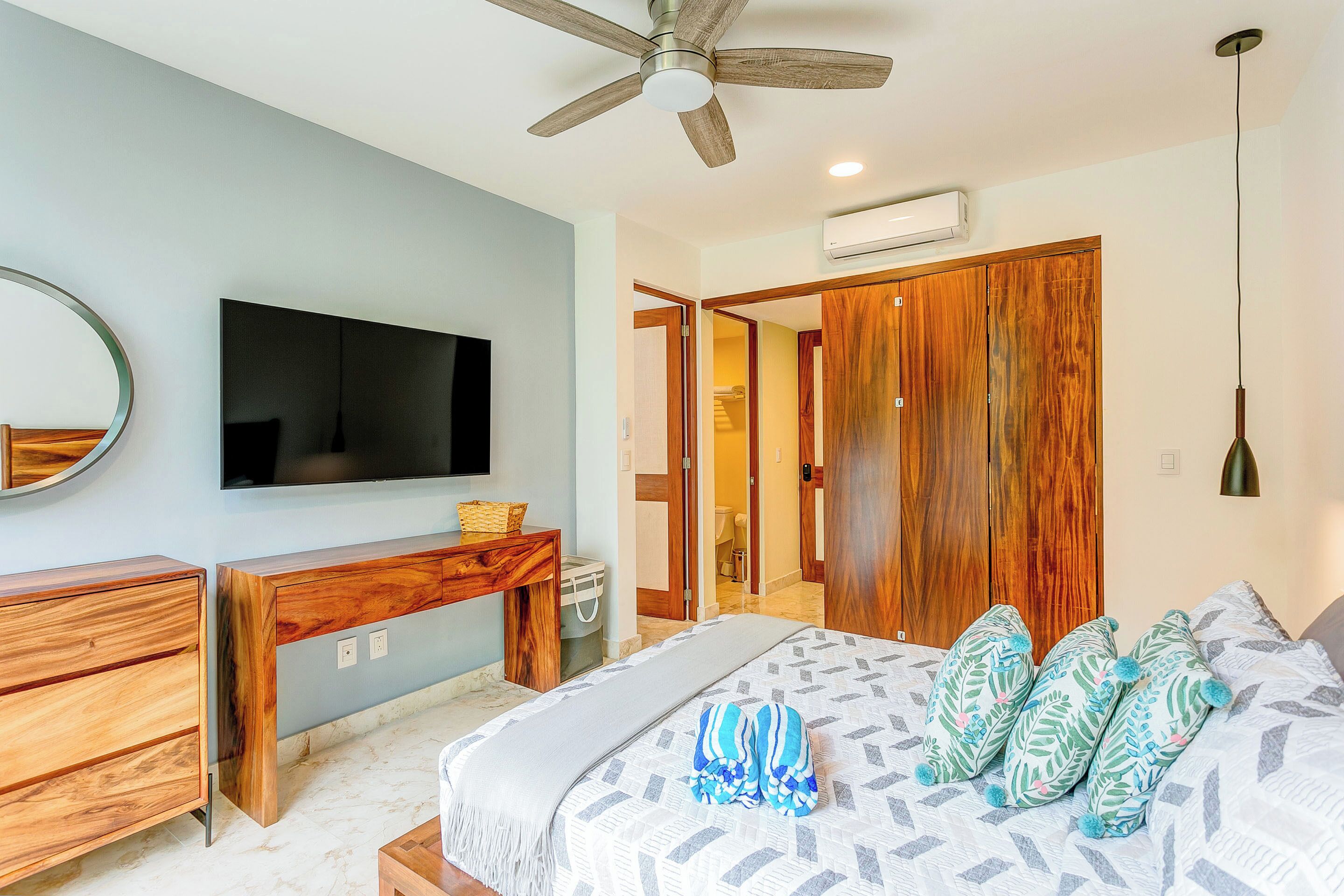 A bedroom with a bed, wooden furniture, a ceiling fan, and a TV on the wall.