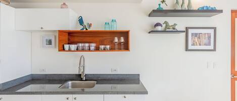 Une cuisine moderne dotée d’un plan de travail en granit, d’un évier en acier inoxydable, de meubles blancs et d’étagères en bois ornées d’objets décoratifs.