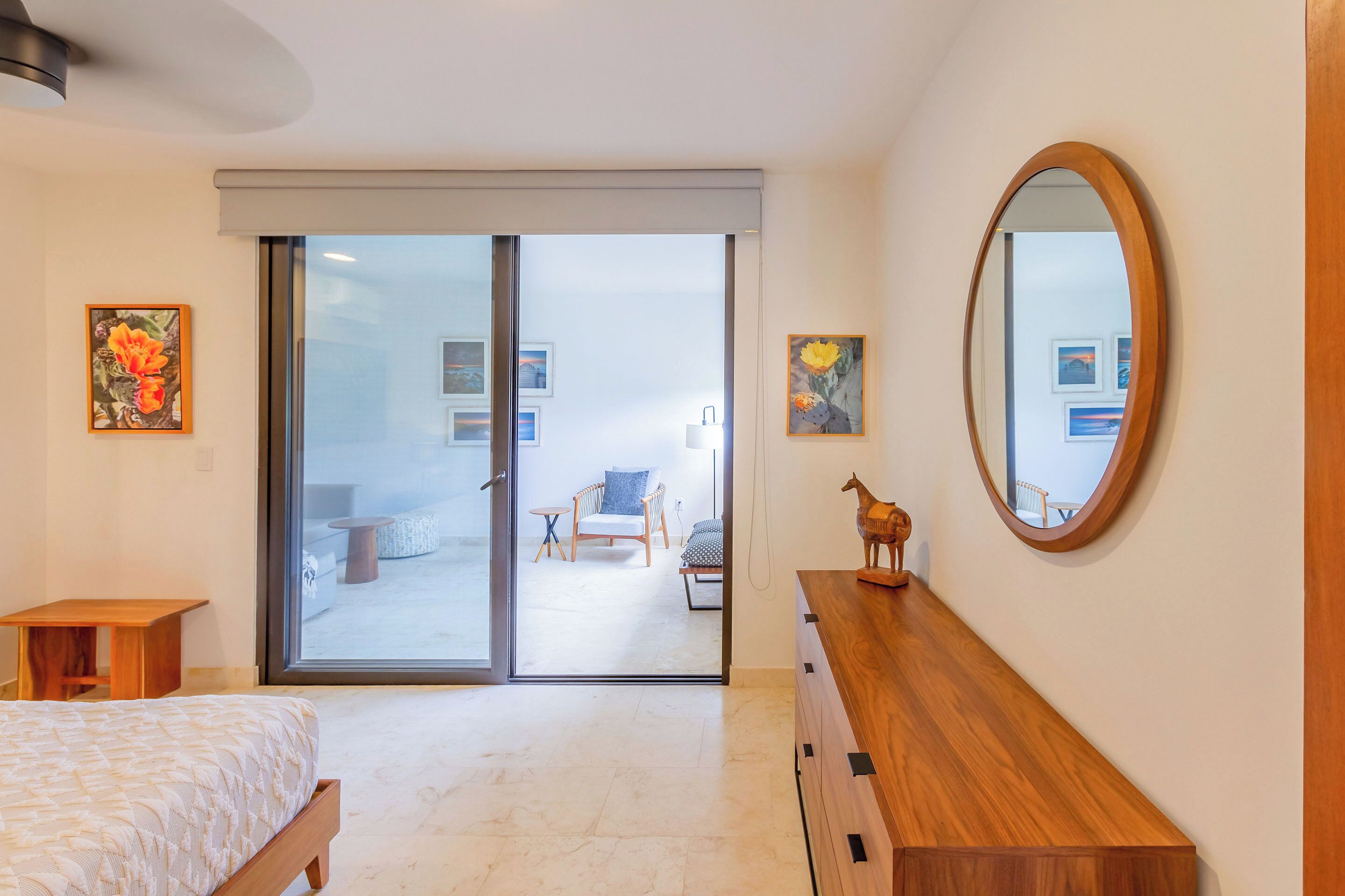 A modern bedroom with a large sliding glass door leading to a balcony, a wooden dresser, and a mirror.