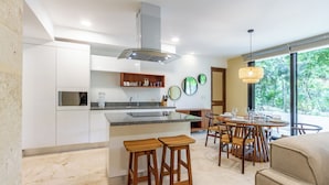 A modern kitchen with a central island, wooden stools, and a dining area with a round table and chairs. - Tropical Retreat Pools Golf Gym  (Akumal)