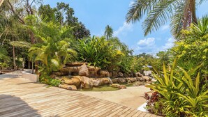 A wooden deck leading to a rock garden with tropical plants and a small water feature. - Tropical Retreat Pools Golf Gym  (Akumal)