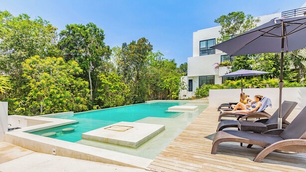 A modern outdoor pool area with lounge chairs and umbrellas, surrounded by lush greenery and a contemporary building. - Tropical Retreat Pools Golf Gym  (Akumal)
