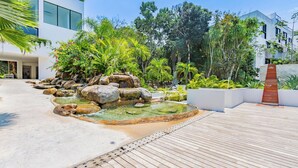 A modern building with a landscaped garden featuring a water feature with rocks and a wooden deck. - Tropical Retreat Pools Golf Gym  (Akumal)