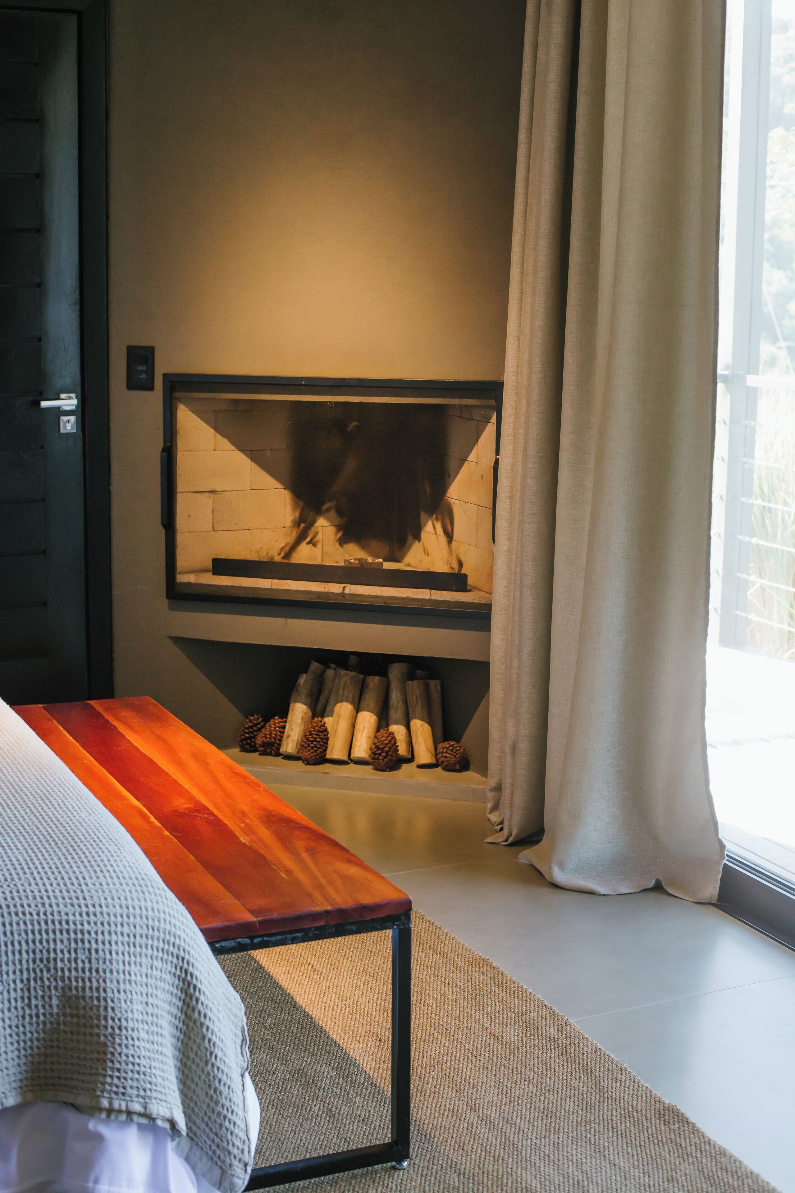 Una habitación con chimenea, un banco de madera y una ventana con cortinas.