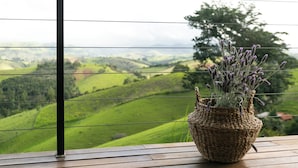 Un florero de mimbre con lavanda sobre una mesa de madera, con vista a colinas verdes y un árbol.