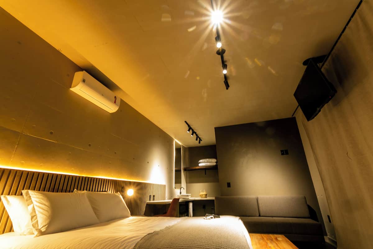 A modern hotel room with a bed, bedside table, and a small seating area.