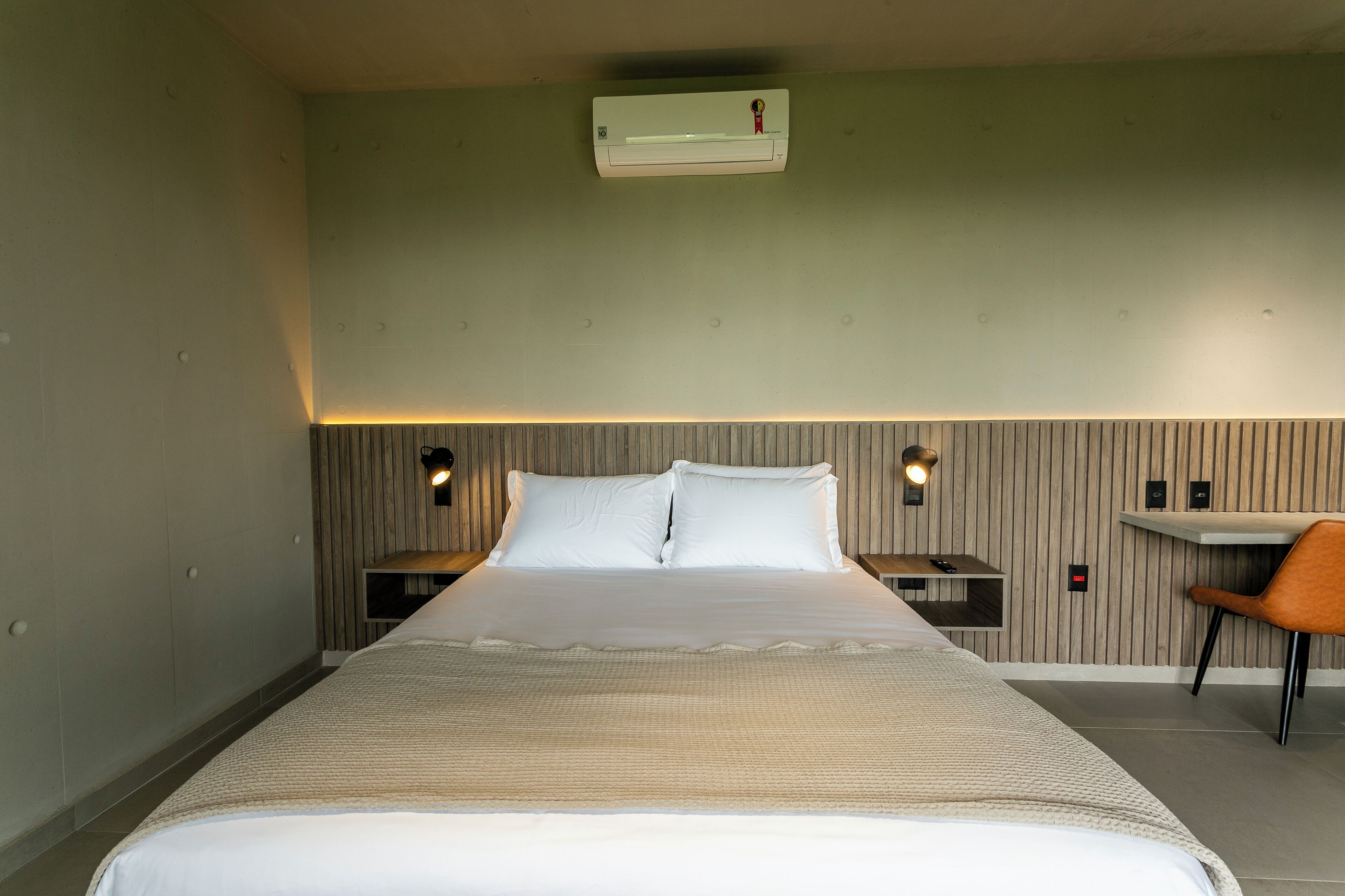 Habitación de hotel con una cama grande, dos mesitas de noche, un escritorio y un aire acondicionado en la pared.